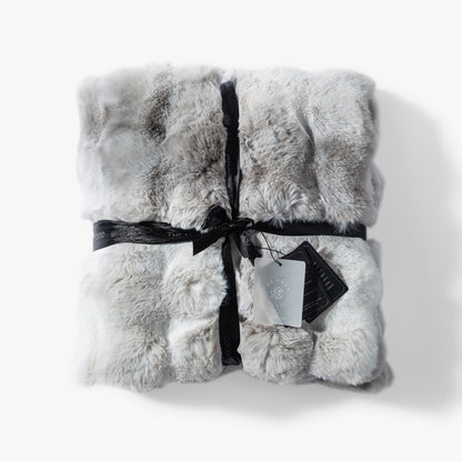 The Mood Cubby 2 faux fur throw in gray and white wrapped in a ribbon with product tags attached, ready for gifting